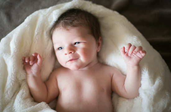 newborn baby boy laying on white blanket slightly smiling