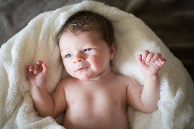 newborn baby boy laying on white blanket slightly smiling