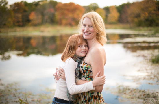 red headed girl hugging her mom near a lake in the fall