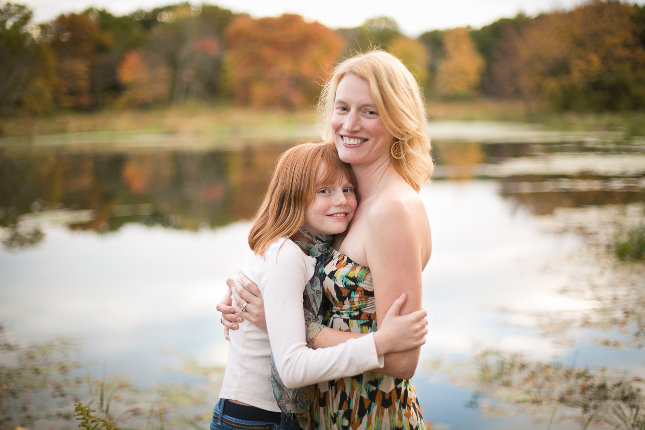red headed girl hugging her mom near a lake in the fall