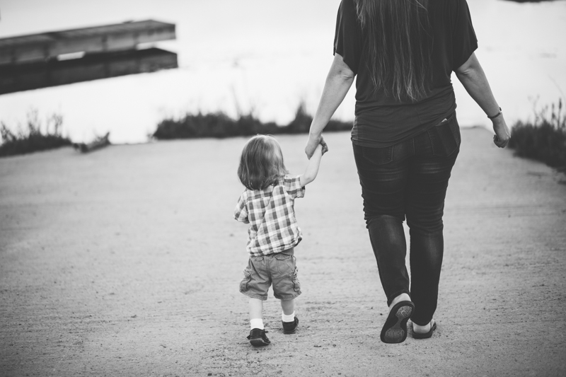 Mom holding baby boys hand walking to water