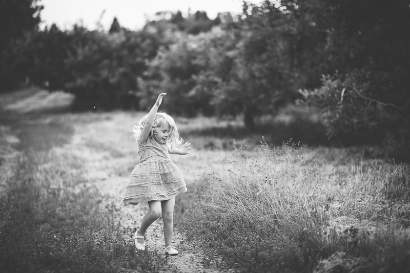 little girl twirling on a dirt road in apple orchard 