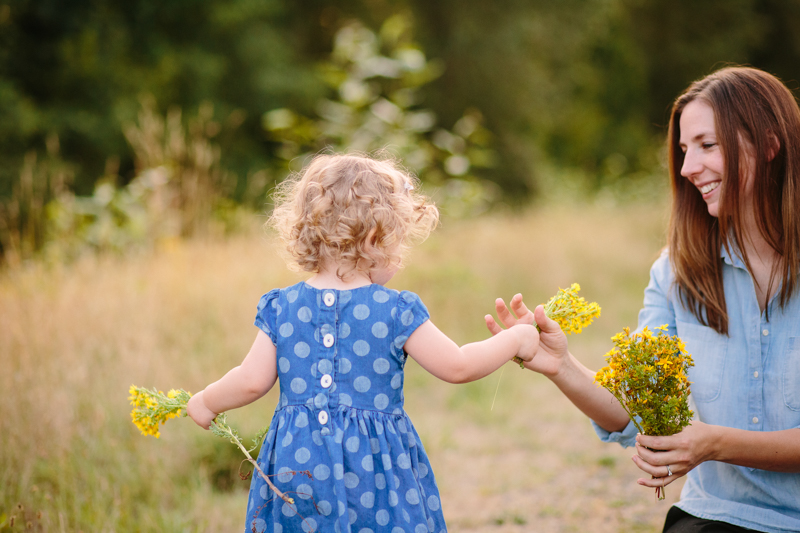 little girl in blue dress handing flowers to mom