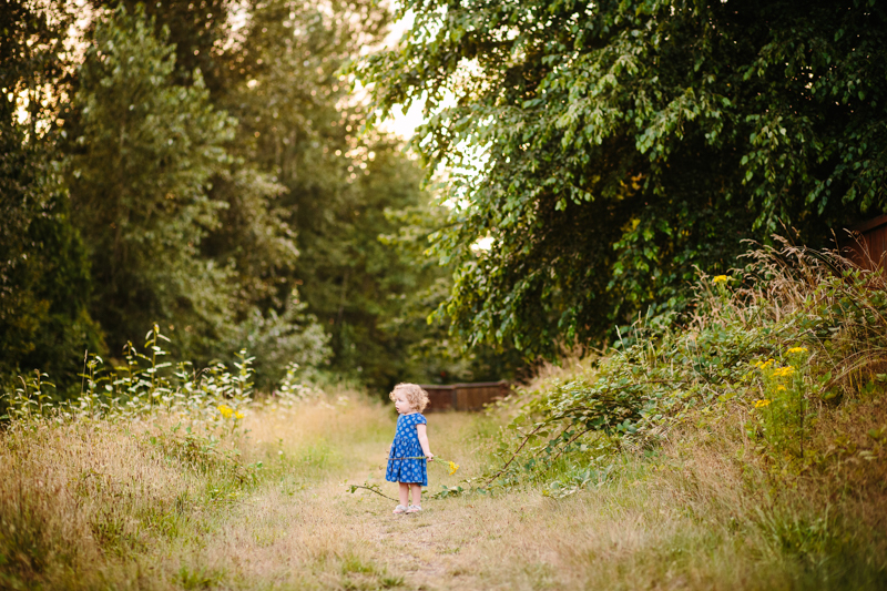 little standing on a trail holding yellow flowers