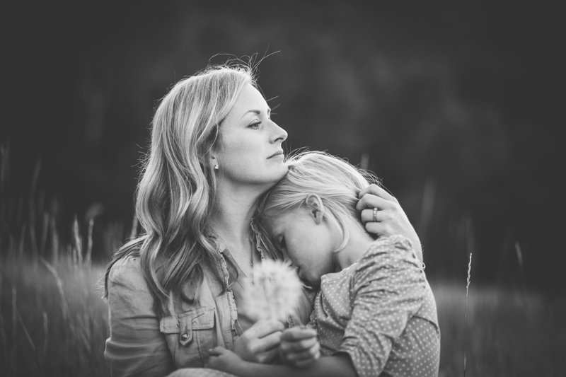 mom snuggling little girl holding dandelion 