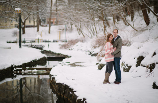 young couple standing in snow near stream