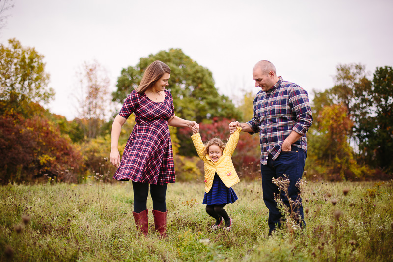 mom and dad swinging little girl in a field
