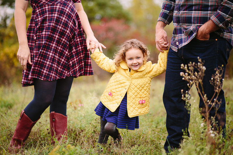 little girl in yellow jacket hold parents hands