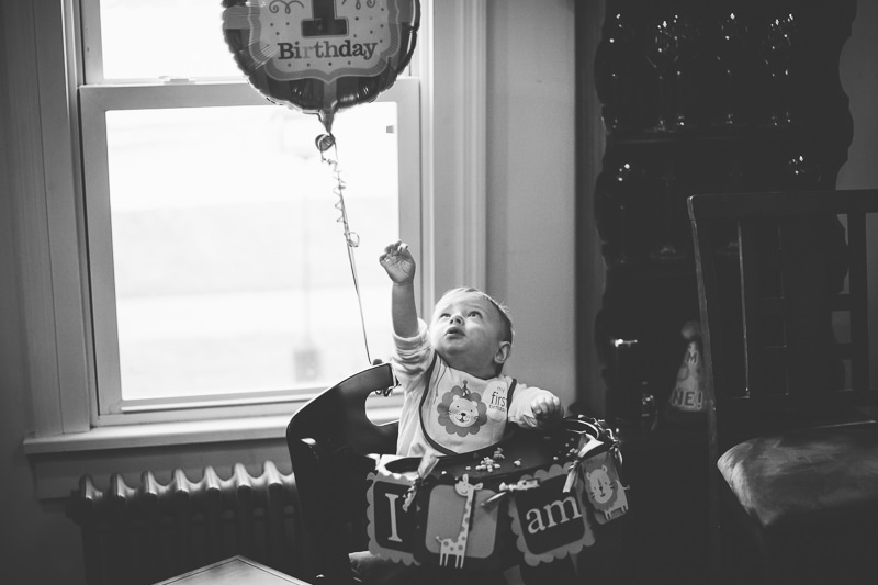 birthday boy in high chair reaching for balloon