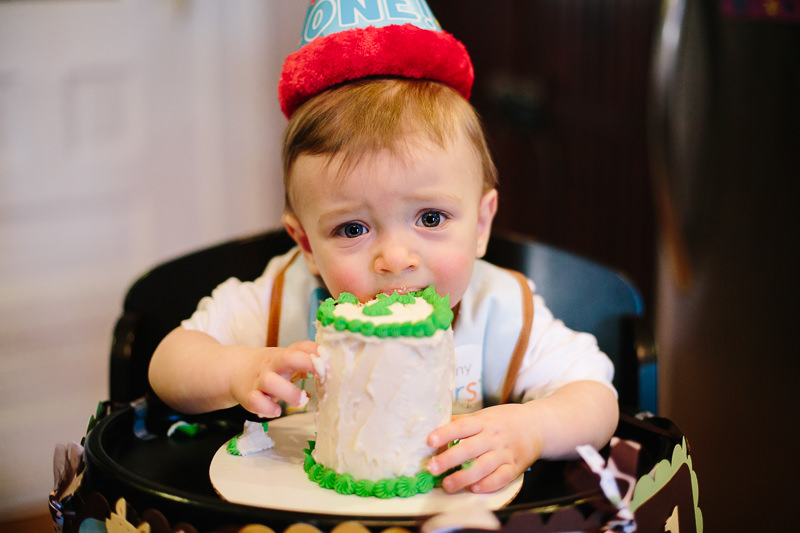 baby boy wearing hat tasting birthday cake