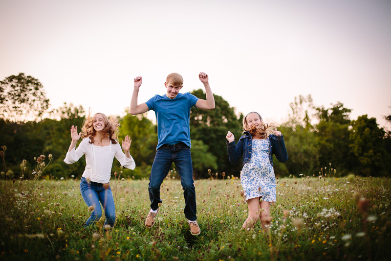 three siblings jumping in the air in a field