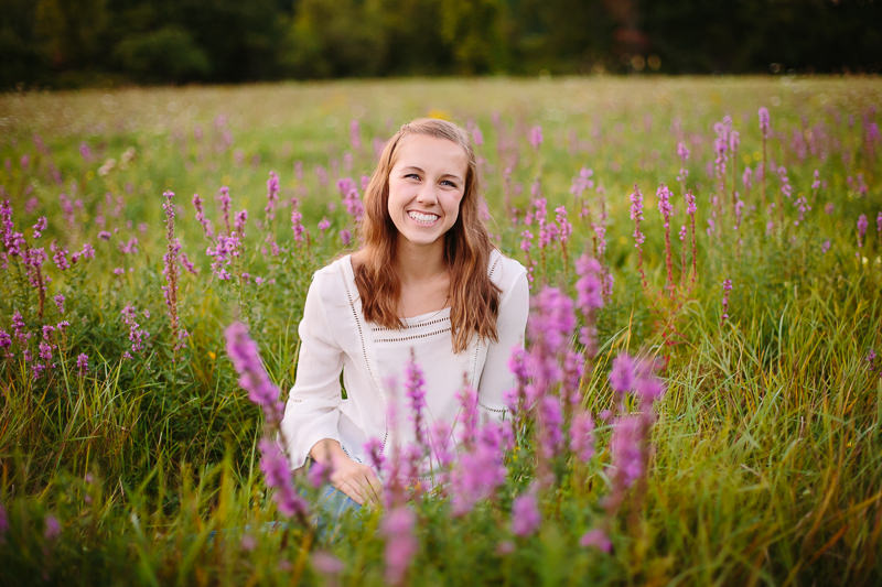 senior girl sitting in a field of purple flowers and grass