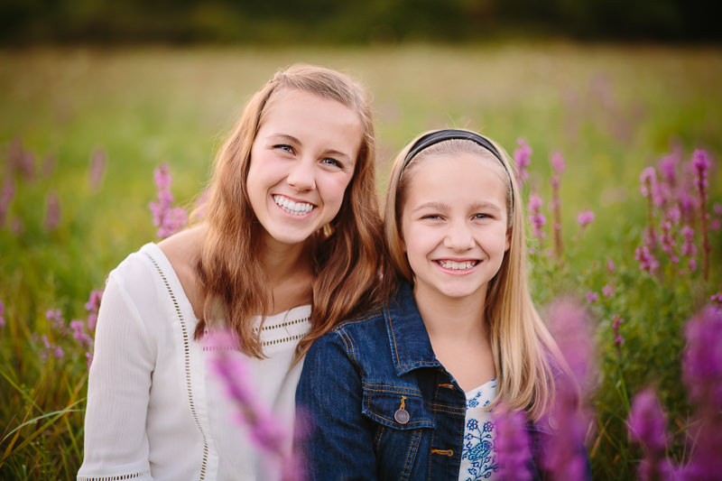 sisters sitting close in a field with purple flowers 