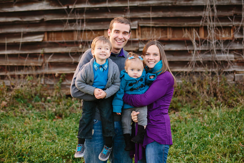 mom dad baby girl and young boy in front of barn