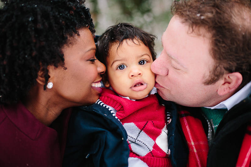black mom and white dad kiss their baby