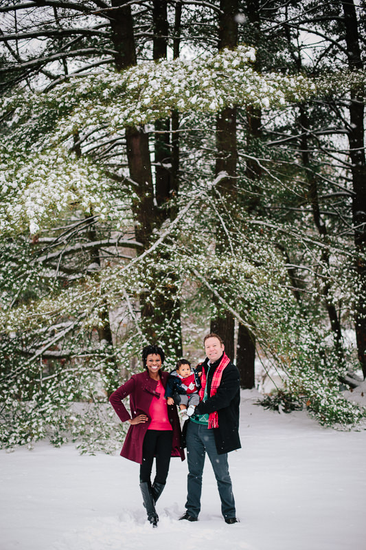 family standing outside in front of large trees with snow