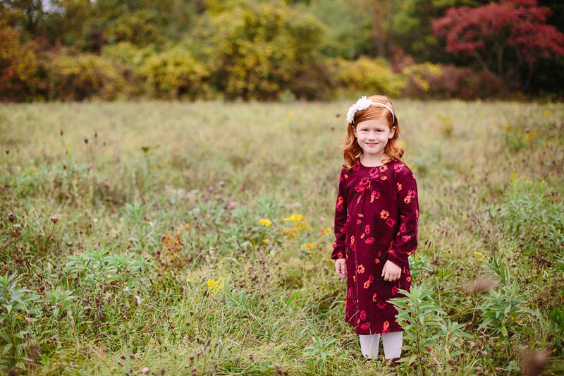 red haired girl with red dress standing in field