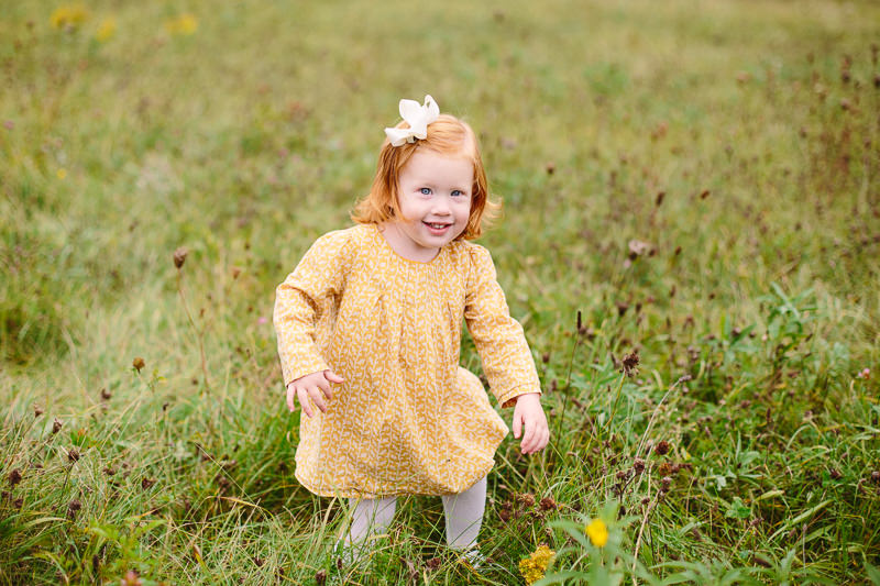 baby girl walking in a field with yellow dress