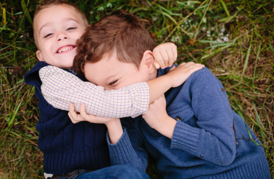 little brother hugging big brother laying on grass