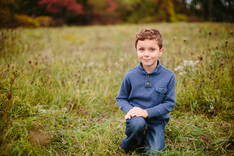 little boy with blue shirt kneeling in grass