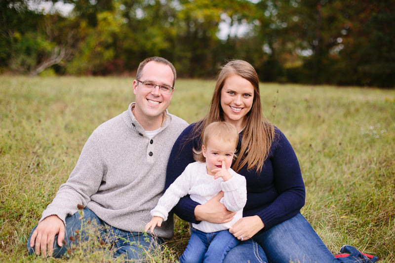 mom dad and baby sitting in a field