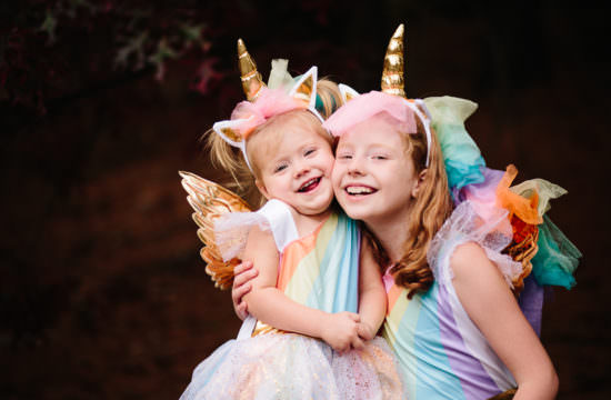 sisters hugging wearing rainbow unicorn costume