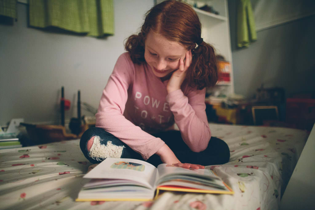 red hair girl in pink shirt reading book