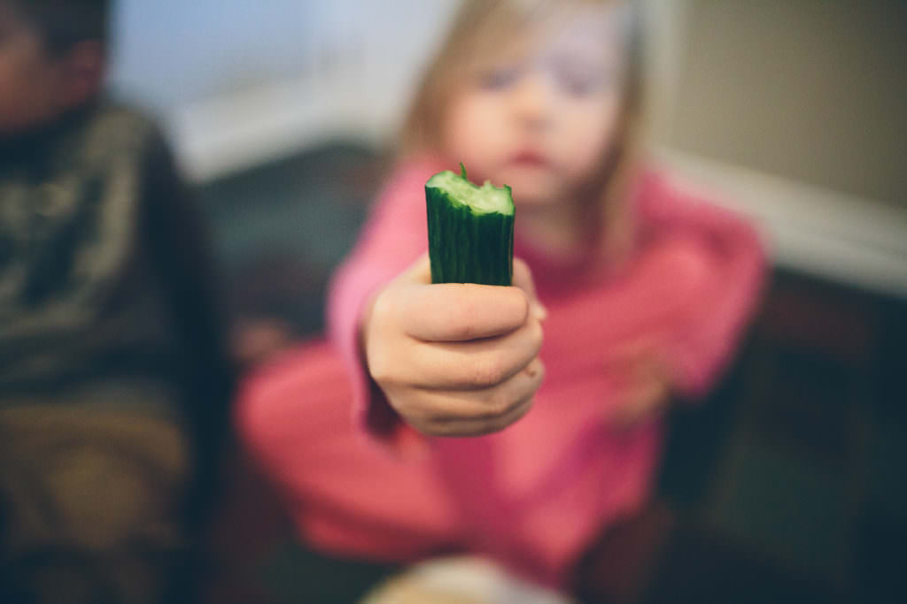 young girl in pink dress holding cucumber