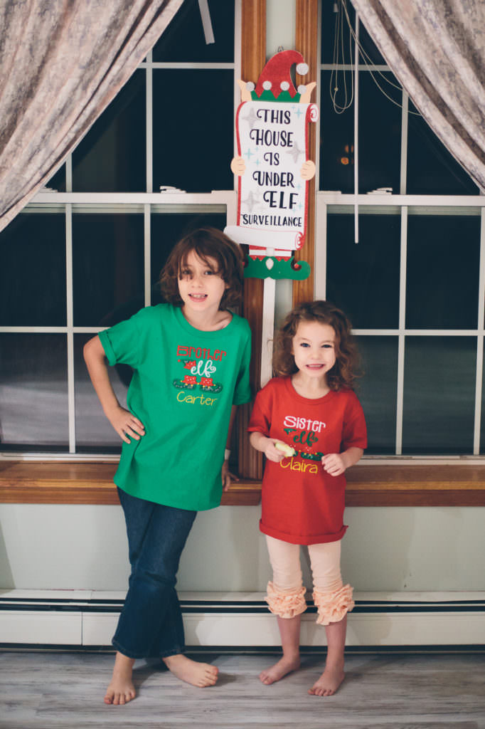 siblings standing before an elf surveillance sign