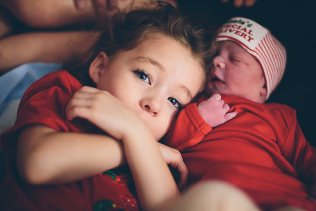 little sister snuggling with new baby brother