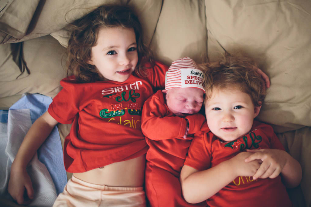 sisters in red snuggling new baby after homebirth