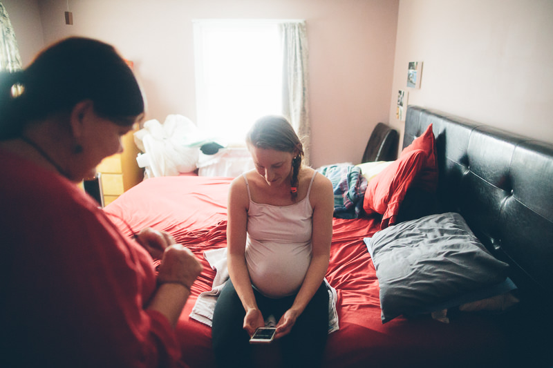 pregnant mom checking phone on bed