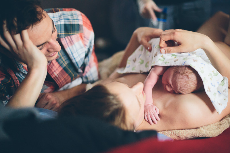 mom and dad lying on bed looking at new baby