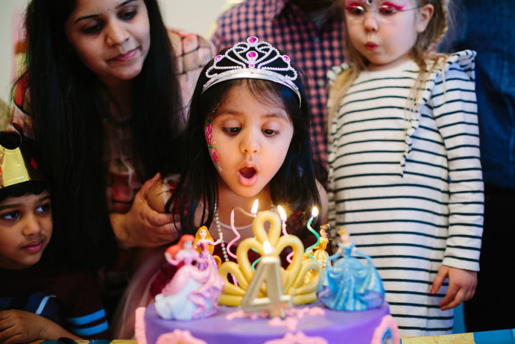 dark haired girl wearing tiara blowing out candles