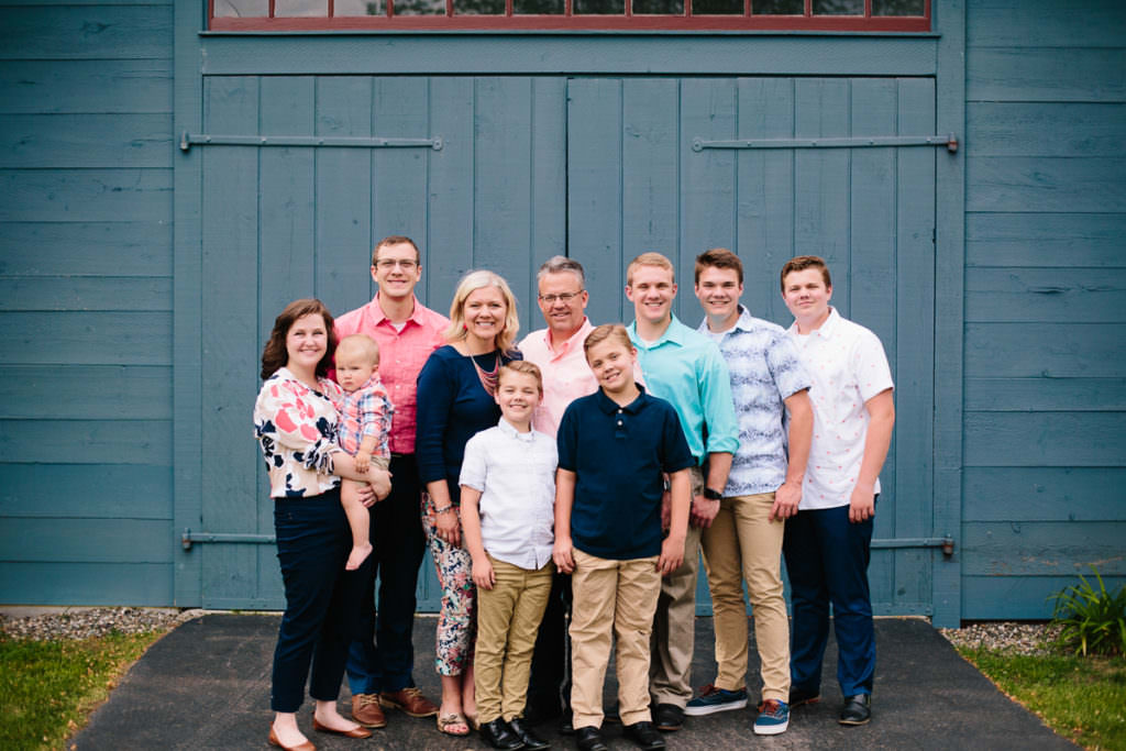 family of ten standing in front of blue barn