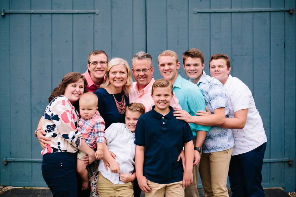 mulitigenerational family standing in front of blue barn