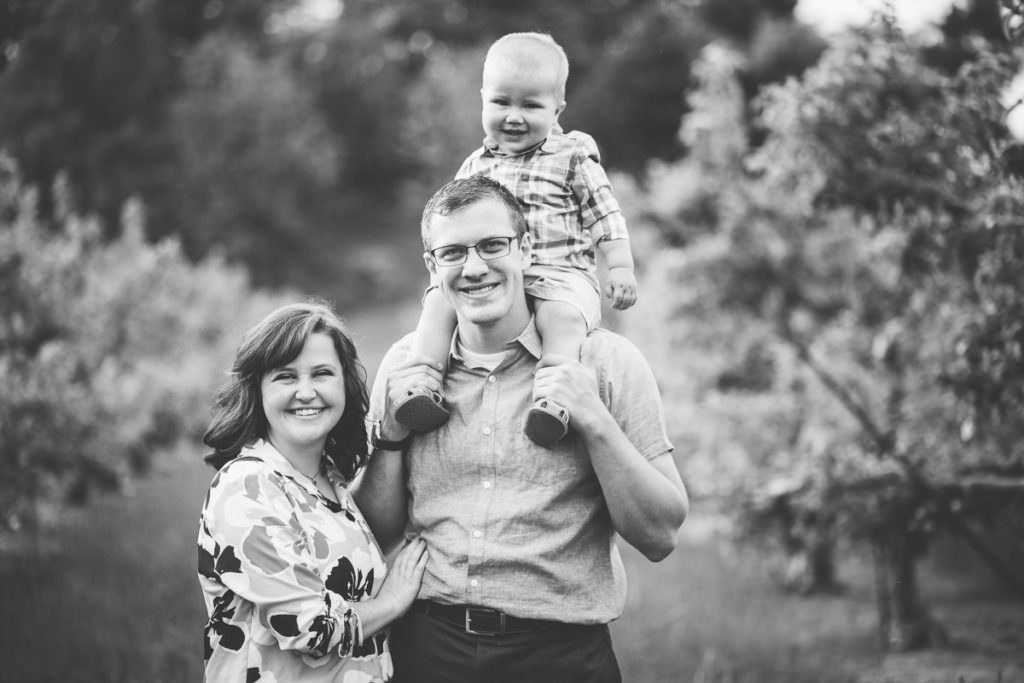 baby boy on dad shoulder in apple orchard