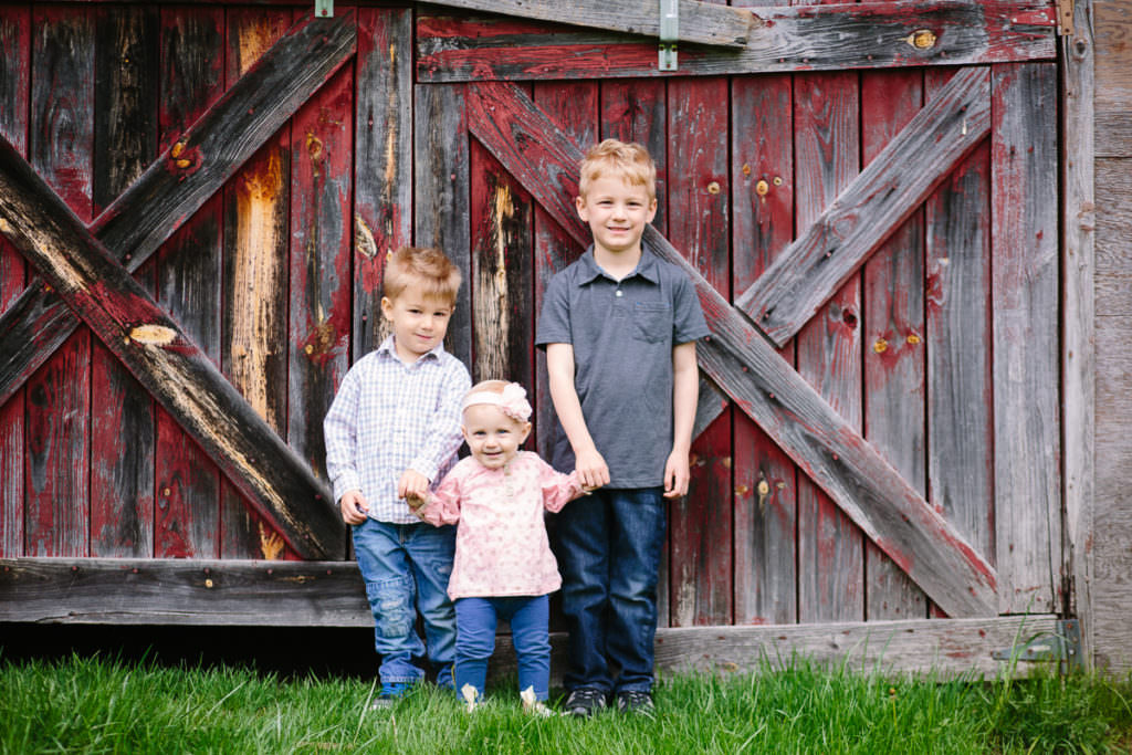 three siblings standing by red barn