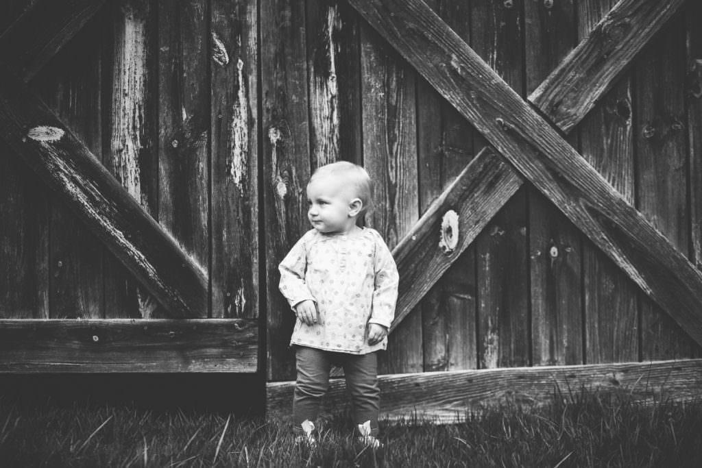 baby girl standing infront of barn