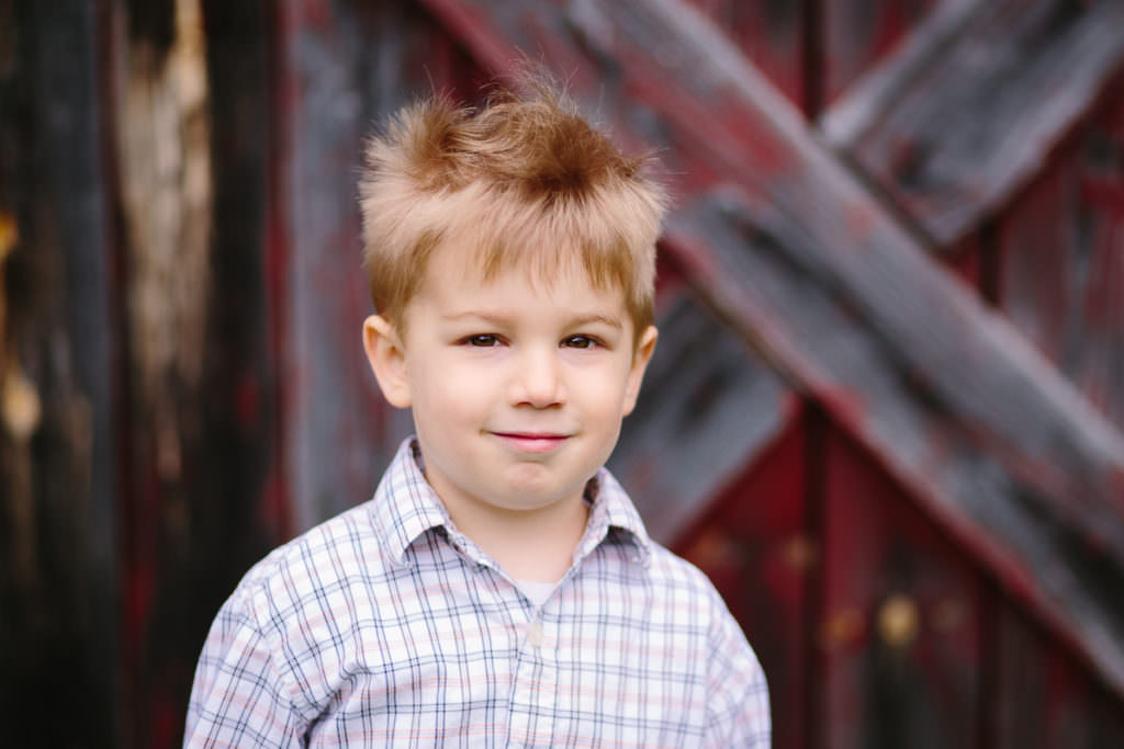 brown hair boy standing infront of barn