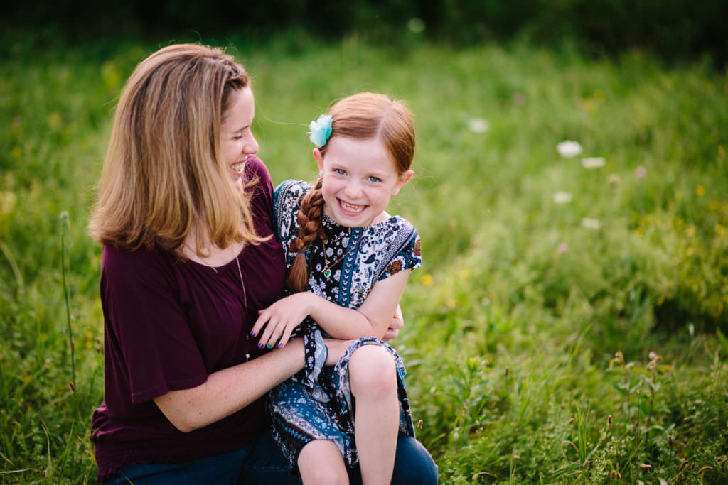 mom tickling daughter in field