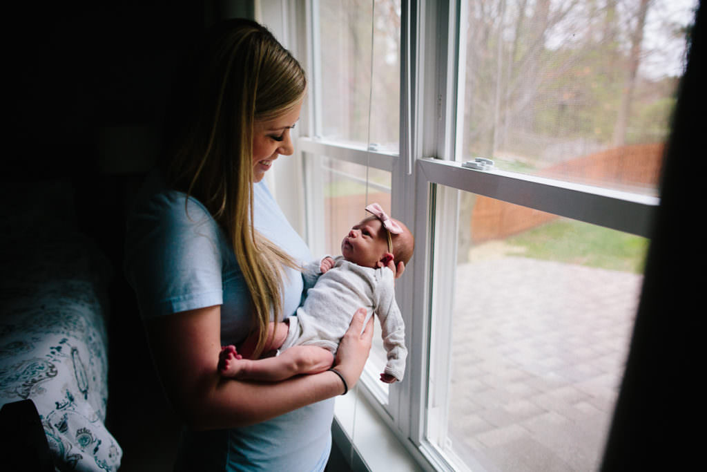 mom smiling at newborn baby by window