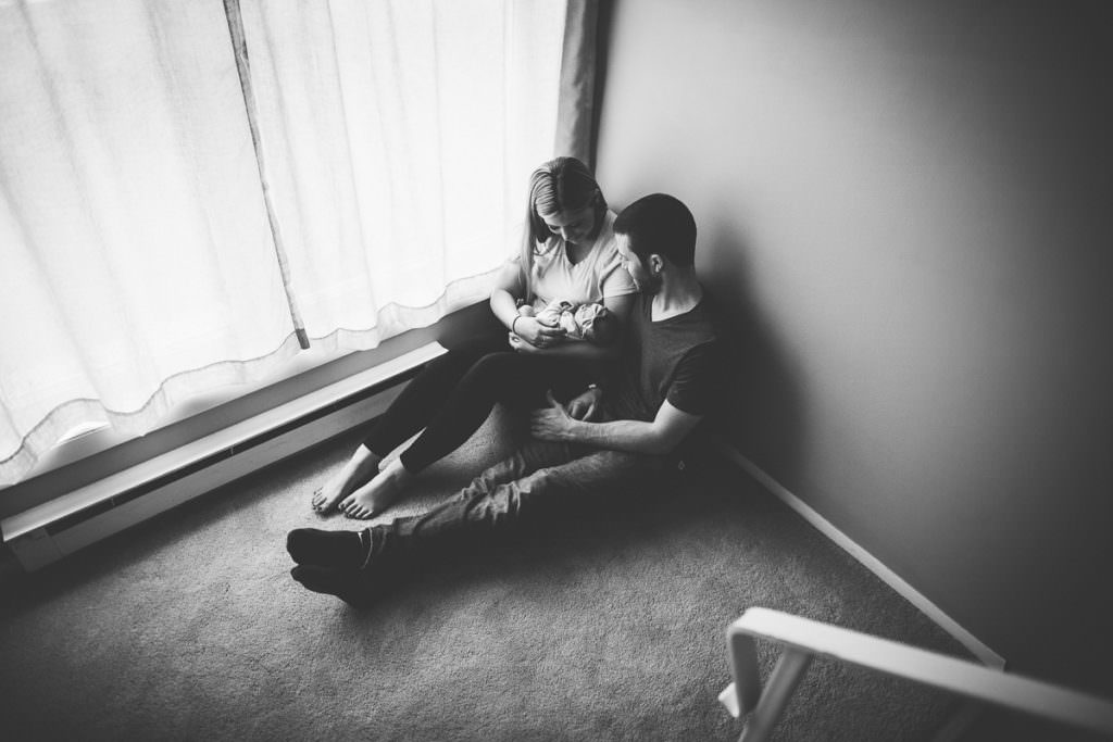 mom and dad holding baby on floor by window