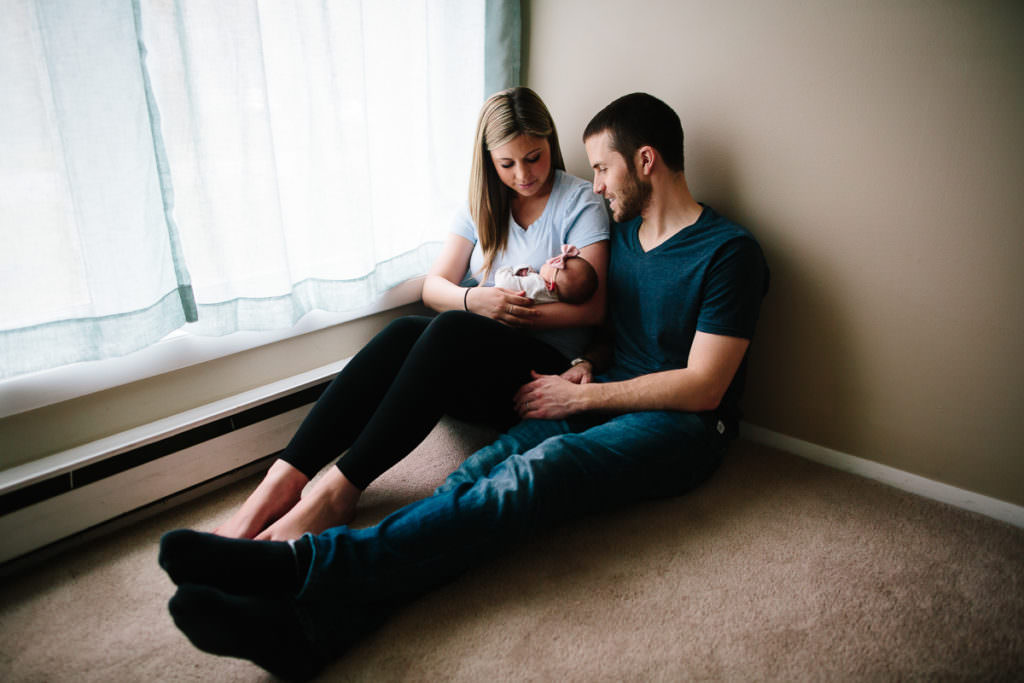 parents holding baby girl on floor by window