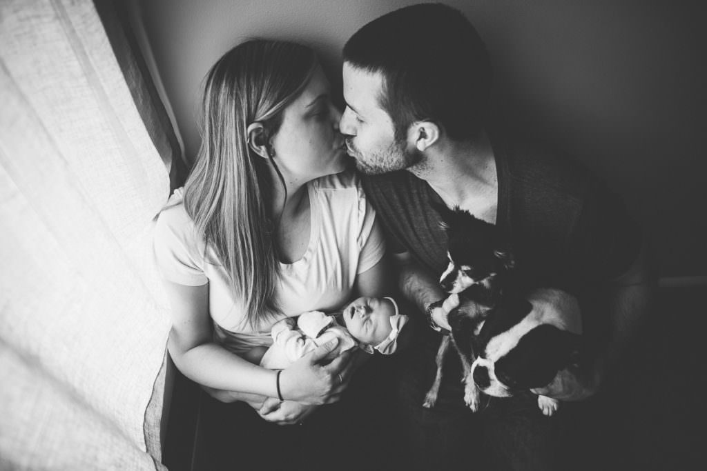 husband and wife kissing holding newborn and dogs