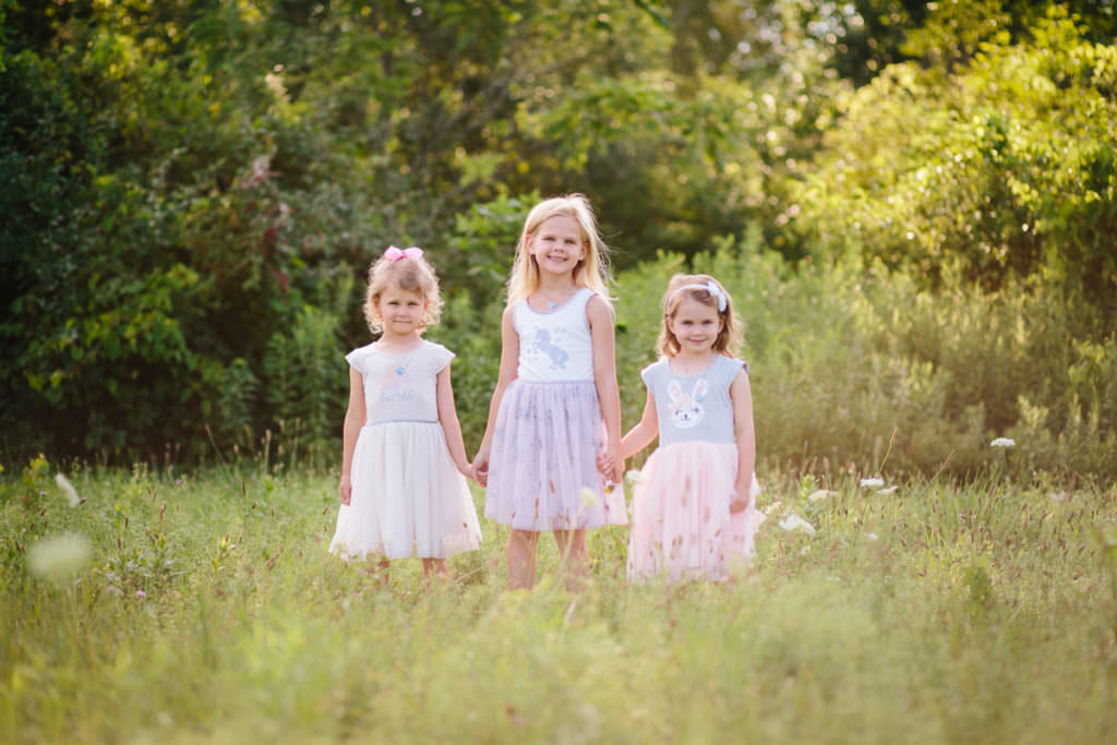 three little girls holding hands in field
