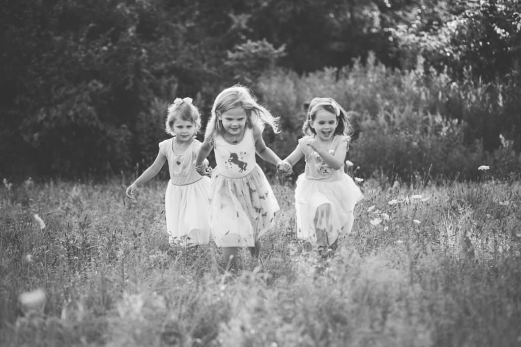 little girls holding hands running in field
