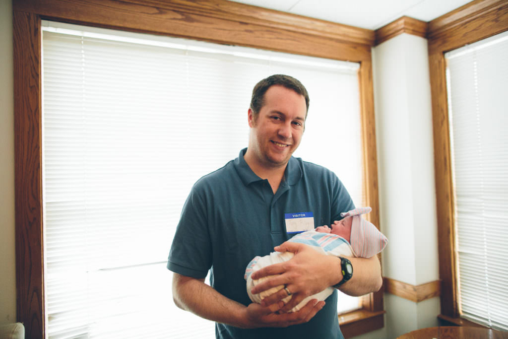 dad holding newborn by hospital window