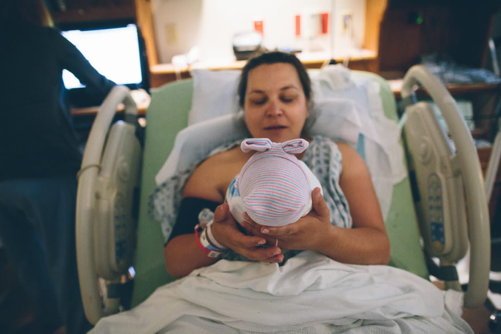 mom holding baby girl in hospital bed with bow hat