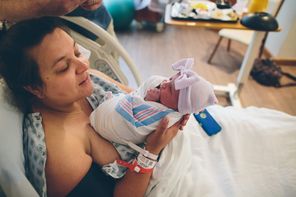 mom holding swaddled baby girl in hospital